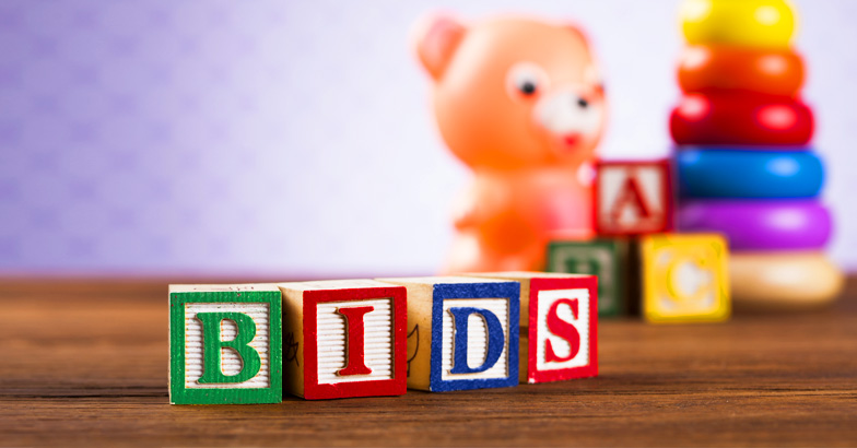 Colourful baby toys including four baby blocks spelling out the word 'bids' - representing Nicole's story on balancing babies and bids.