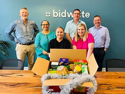 BidWrite Perth staff with Christmas-themed foodbank donations as part of a community impact initiative.