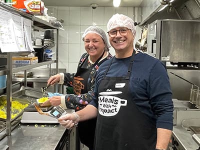 BidWrite employees Kelly & Mark volunteering in the kitchen at Meals for Impact as part of a community impact initiative.