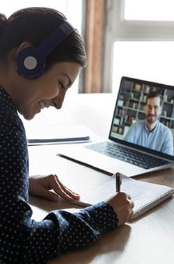 Woman attending one of BidWrite's free webinars on her laptop, smiling and taking notes.