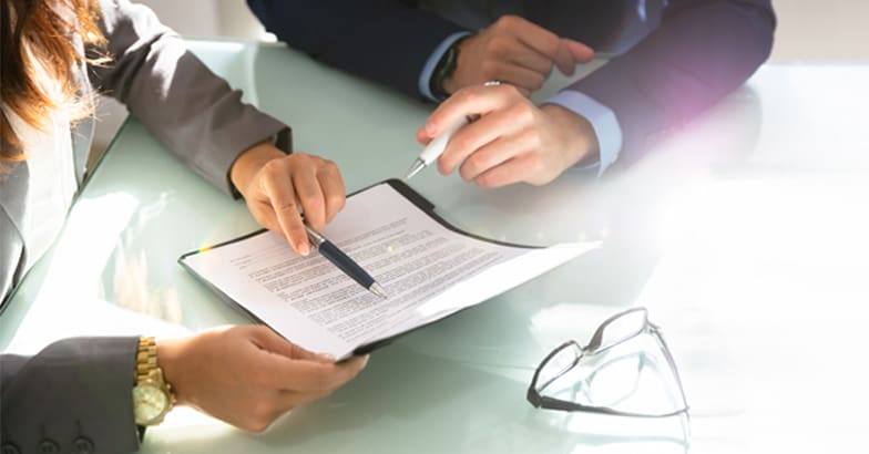 Businessman and businesswoman sitting at office desk with documents conducting tender reviews together.