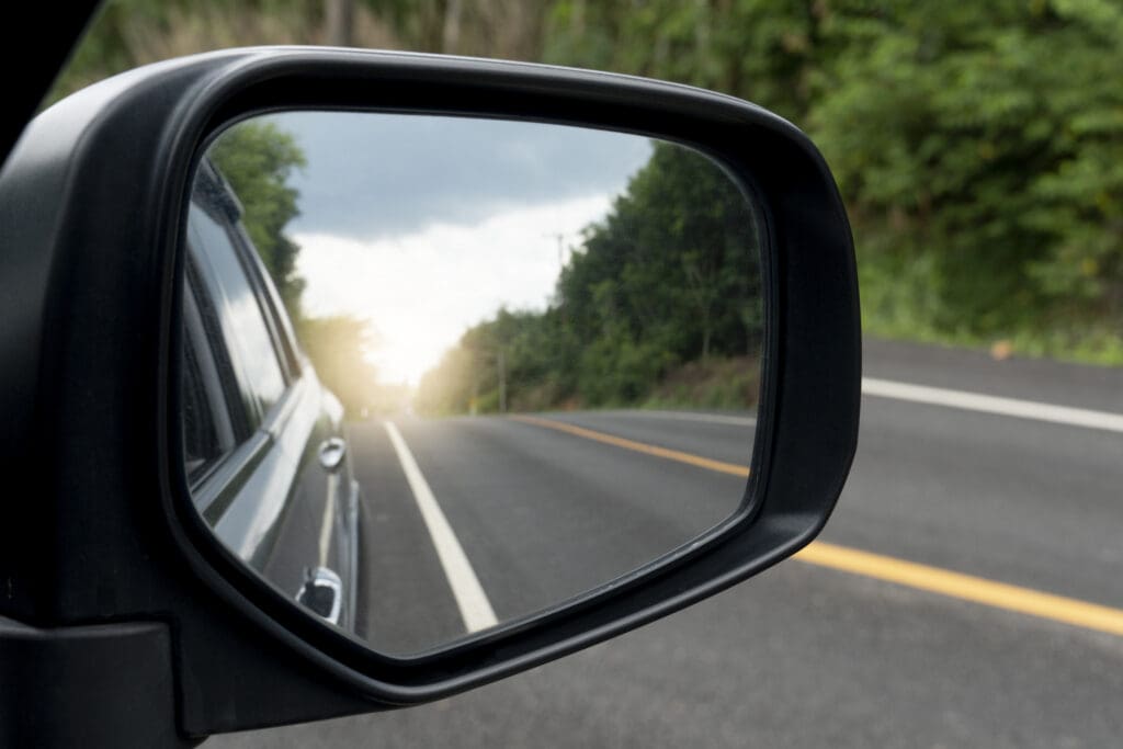 A car side mirror looks back on a long road, surrounded by forest, representing reflecting on change in the tendering industry.